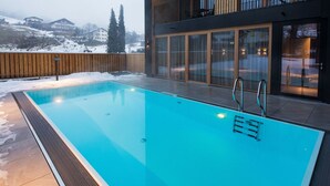 Ein moderner Außenpool mit Holzterrasse und Blick auf einen verschneiten Berg.