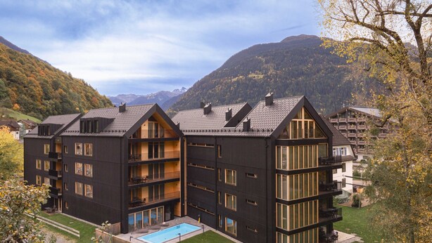 Ein modernes, mehrstöckiges Hotel mit Pool, Balkonen und einer Bergkulisse.