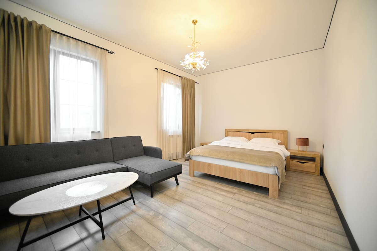 A modern bedroom with a wooden bed, a grey sofa, and a small table.