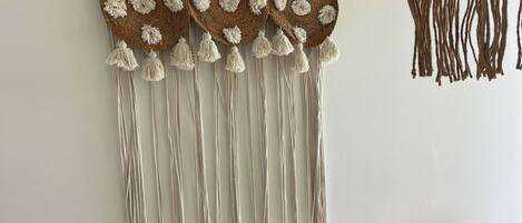 A bedroom with a macrame wall hanging, two brown pillows, and a white bedspread.