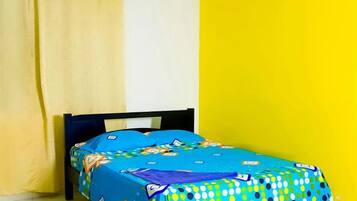 Una cama con una colcha colorida, una cortina y una pared amarilla.