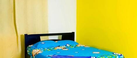 A bed with a colorful bedspread, a curtain, and a yellow wall.
