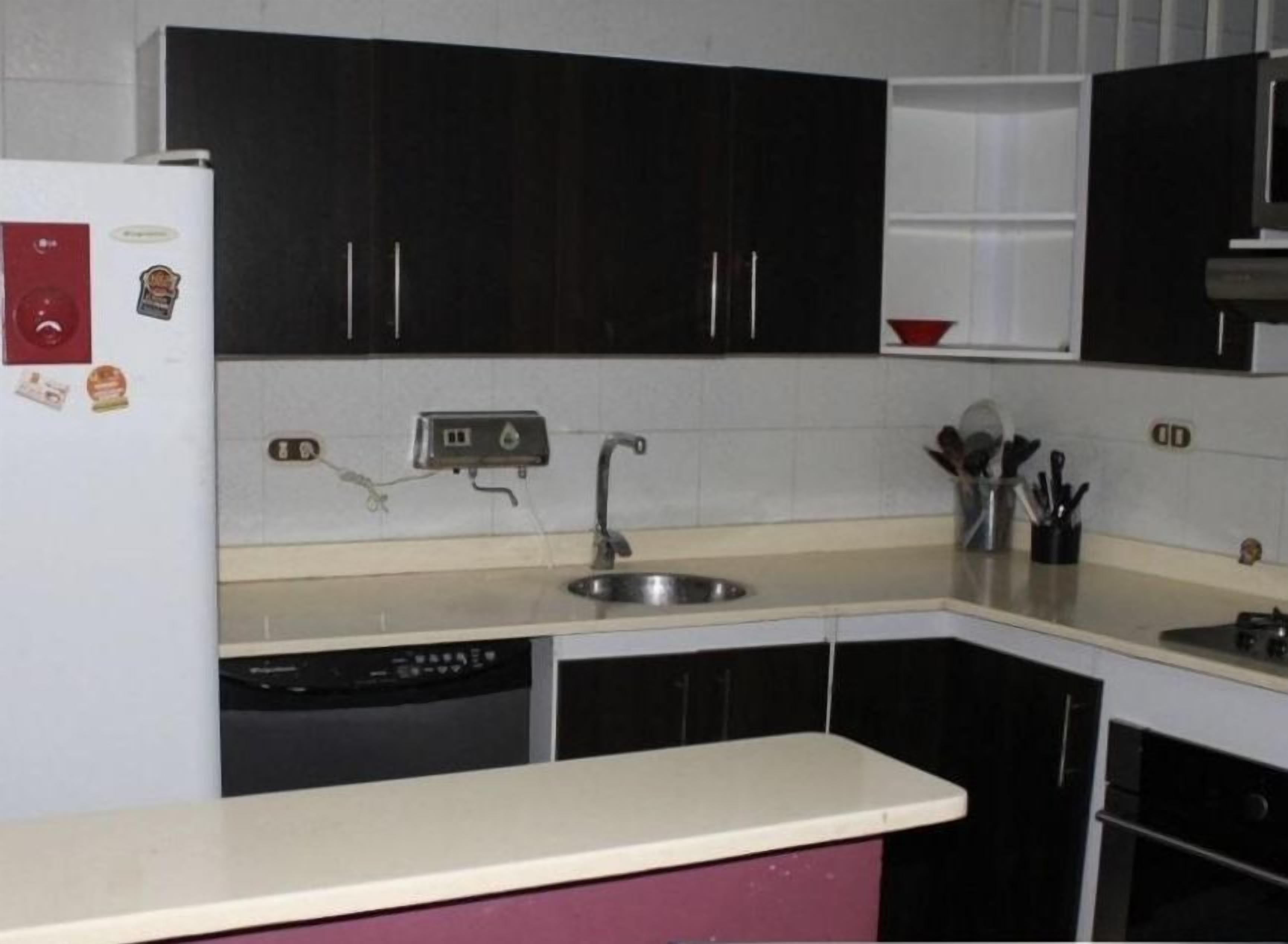 Una cocina con gabinetes negros, encimera blanca, un lavabo y lavavajillas.