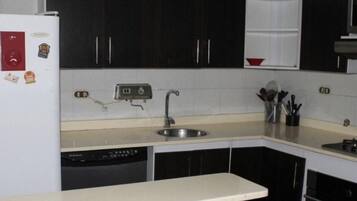 Una cocina con gabinetes negros, encimera blanca, un lavabo y lavavajillas.