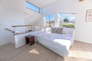 Une chambre à coucher avec un lit, une petite table de chevet en bois, une fenêtre donnant sur l’extérieur et une lucarne.