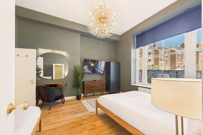 Un dormitorio moderno con cama, escritorio, televisor y una ventana grande con vista a edificios.