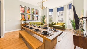 Un moderno comedor con una larga mesa de madera dispuesta para seis comensales, un sofá verde y un amplio ventanal con vistas a la ciudad.