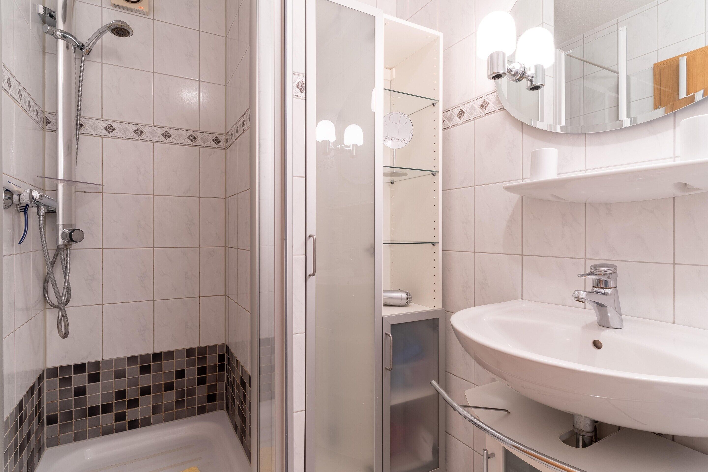 A modern bathroom with a glass-enclosed shower, a white sink, and a mirror above it.