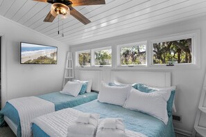 Une chambre avec deux lits, une télévision et des fenêtres donnant sur les arbres et la plage.