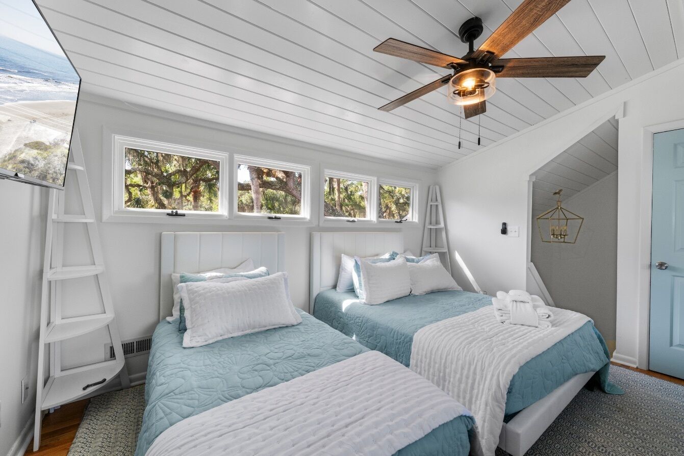 A bedroom with two beds, a ceiling fan, and a view of the outdoors.