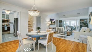 A modern kitchen with stainless steel appliances, a dining area with a round table and chairs, and a living room with a sofa and a TV.
