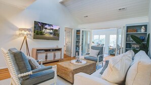 A spacious living room with a high ceiling, a large TV mounted on the wall, and a comfortable seating area with a sofa and chairs.