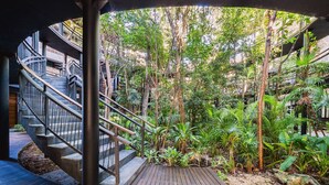 A wooden deck with a spiral staircase leading to an upper level, surrounded by lush greenery and trees. - Romantic Garden Apt w Private Pool | SPA Access (Tulum)
