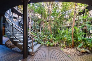 A wooden deck with a spiral staircase leading to an upper level, surrounded by lush greenery and trees. - Romantic Garden Apt w Private Pool | SPA Access (Tulum)