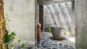 Un intérieur revêtu de pierres, agrémenté d’un grand bac à plantes en béton et d’un tabouret en bois rustique.