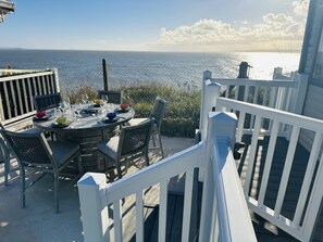 A deck with a table set for dining, overlooking the ocean.
