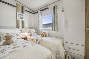 Une chambre avec deux lits, une fenêtre avec des rideaux, une table de chevet avec une lampe et un tableau accroché au mur.