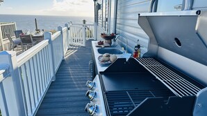 A deck with a grill, sink, and dining area overlooking the sea.