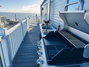 A deck with a grill, sink, and dining area overlooking the sea.