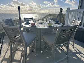 An outdoor dining area with a round table set for two, surrounded by chairs, overlooking a scenic view.