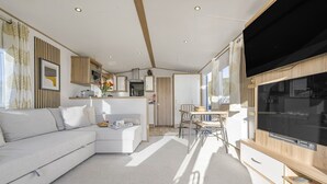 A modern living room with a sofa, a dining table with chairs, a TV, and a kitchen area with cabinets and a microwave.