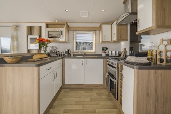 A modern kitchen with wooden cabinets, a built-in microwave, a stove, and a sink. - Seaviews Porthkerry Holiday Park Sleeps 6 (Barry)
