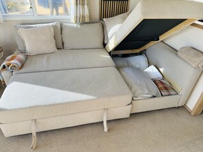 Un canapé convertible doté d’un espace de rangement intégré, une fenêtre avec des rideaux et un sol recouvert d’une moquette.