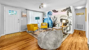 Una sala de estar moderna con piso de madera, un sillón informal grande color gris, sillas amarillas y un mural de un flamenco.
