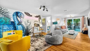 Una sala de estar moderna con un mural vibrante, un sofá amarillo, un sillón de peluche gris y suelo de madera.