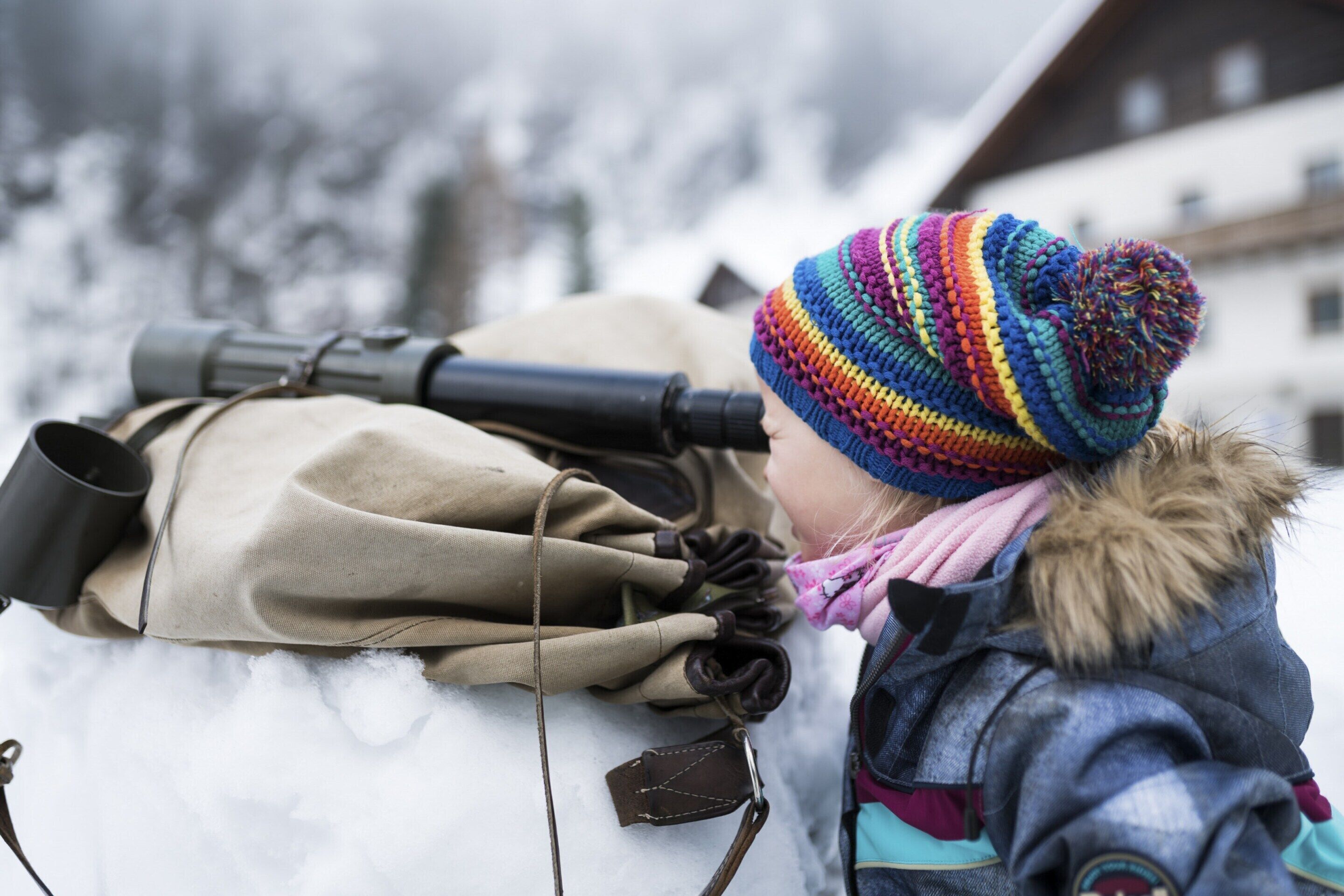 A person lying on the snow with a backpack and binoculars.
