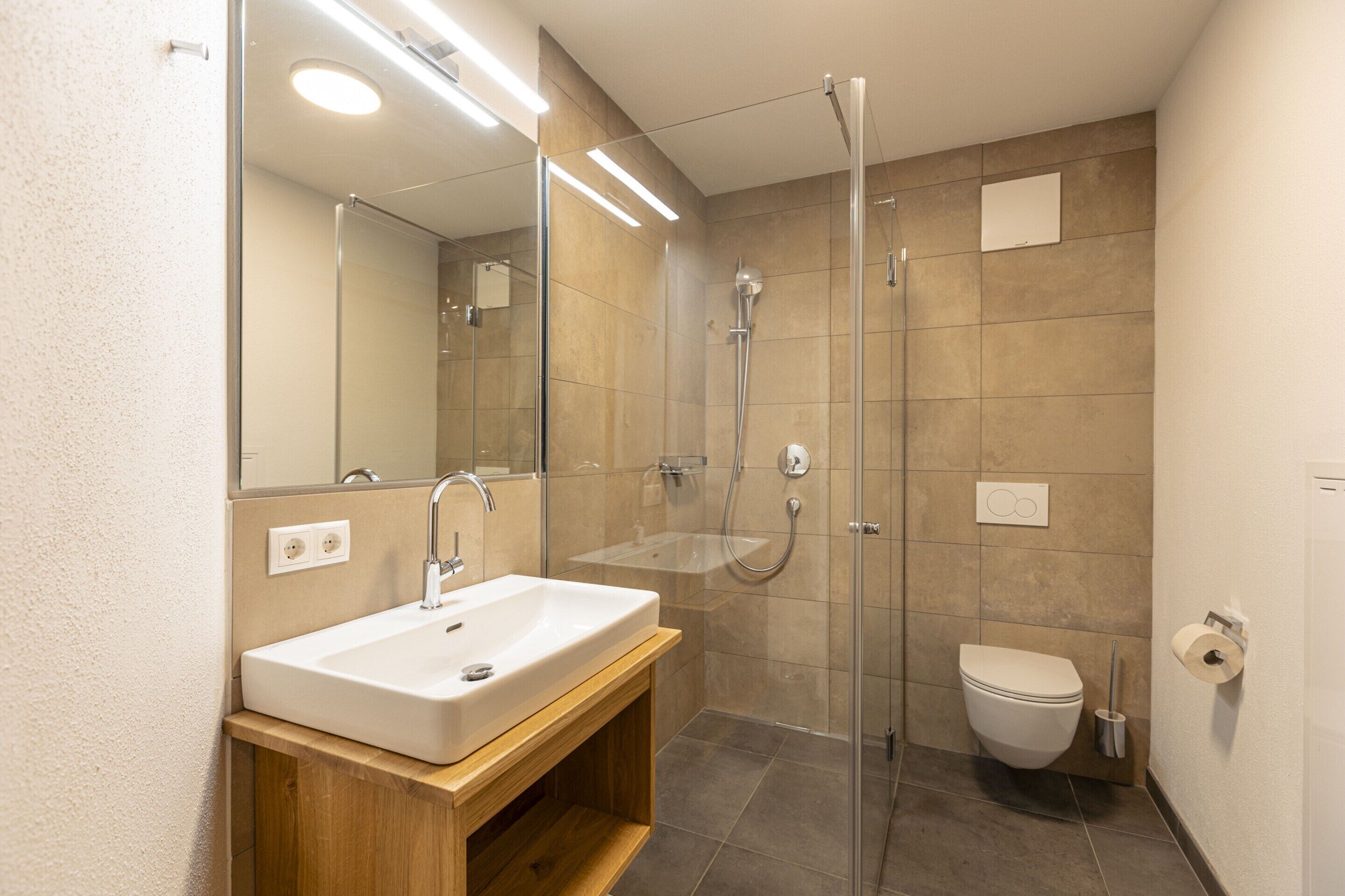 Ein modernes Badezimmer mit Waschbecken, Spiegel, Dusche und Toilette.