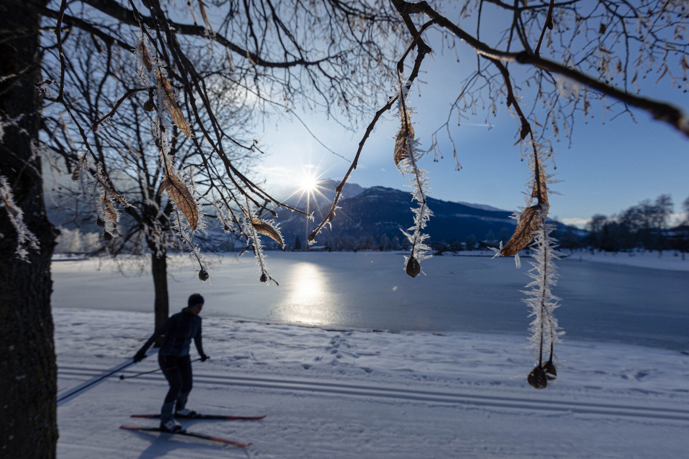Henkilö hiihtää maastossa, ja maisemassa näkyy lumipeitteinen reitti, järvi ja vuoret.