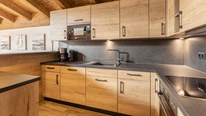 A modern kitchen with wooden cabinets, a stainless steel sink, and a built-in oven. - Superior Ferienhaus # 4C mit Sauna (Uttendorf)