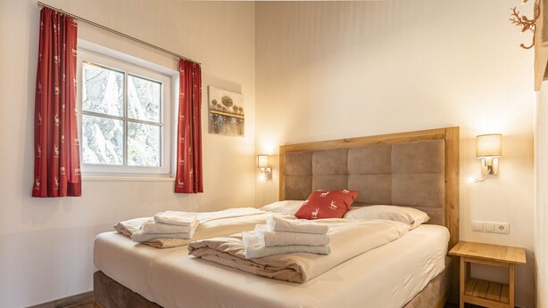 Quarto com uma cama grande, duas mesas de cabeceira, uma janela com cortinas e um abajur fixado na parede.