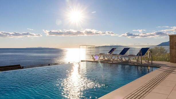 A pool with lounge chairs and a glass barrier overlooking a body of water and distant mountains. - Luxury Villa with pool and panoramic sea view! (Potomje)