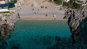 An aerial view of a beach with clear turquoise water, rocky cliffs, and a few people scattered across the sand. - Luxury Villa with pool and panoramic sea view! (Potomje)