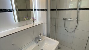 Een moderne badkamer met een witte wastafel, spiegel en douche.