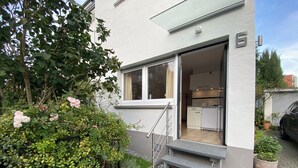 Een modern gebouw met een witte gevel, een zichtbare keuken en een klein buitenterrein met trappen naar de ingang.