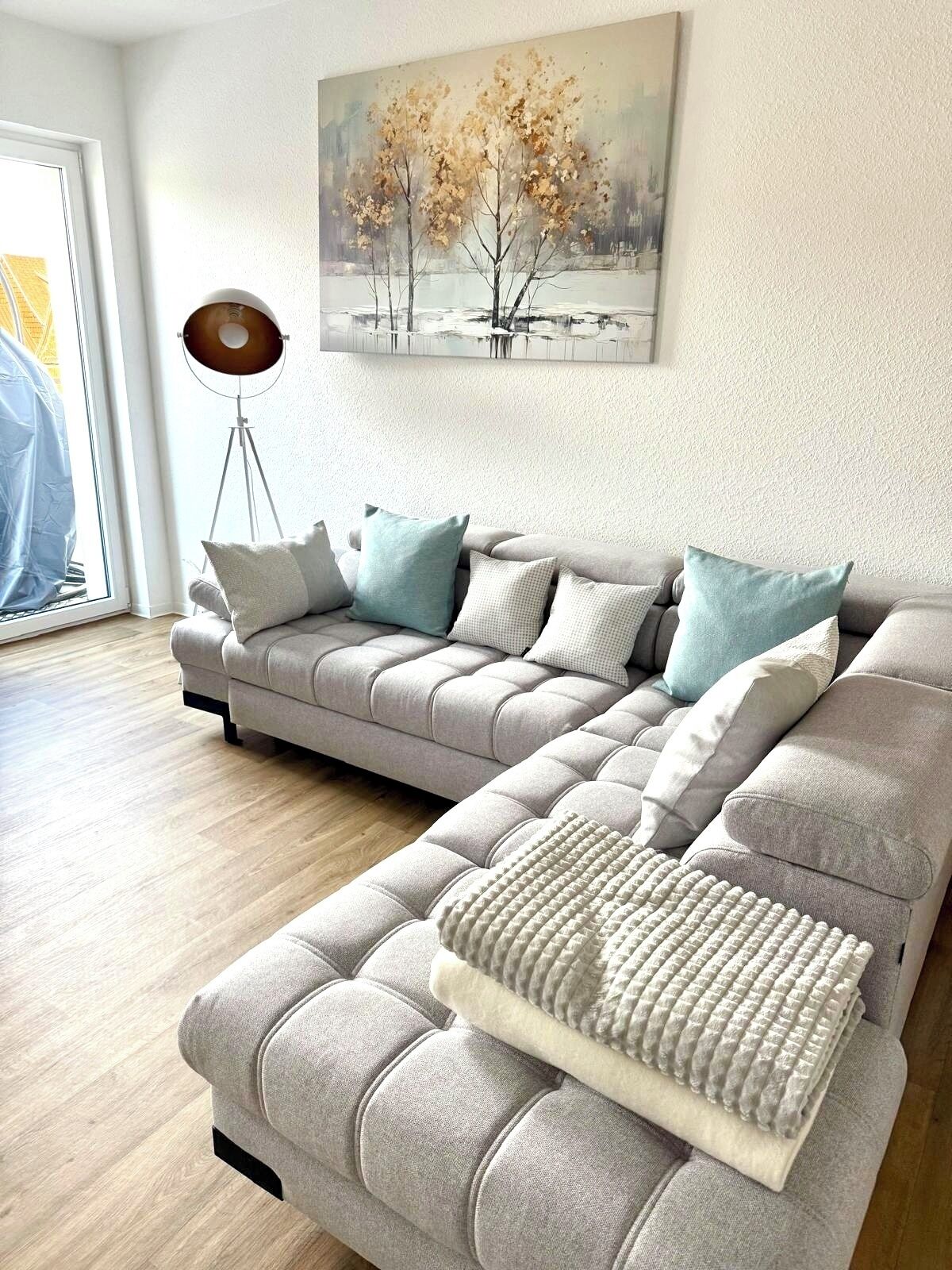 Ein modernes Wohnzimmer mit einer Eckcouch, einer Stehlampe und einem Gemälde an der Wand.