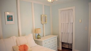 Een slaapkamer met een bed, een dressoir, een spiegel en een raam met gordijnen.