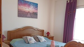 A bedroom with a wooden bed, a nightstand, a lamp, a painting of a beach scene, and purple curtains. - Adorable Home With Swimming Pool and sea View (Senj)
