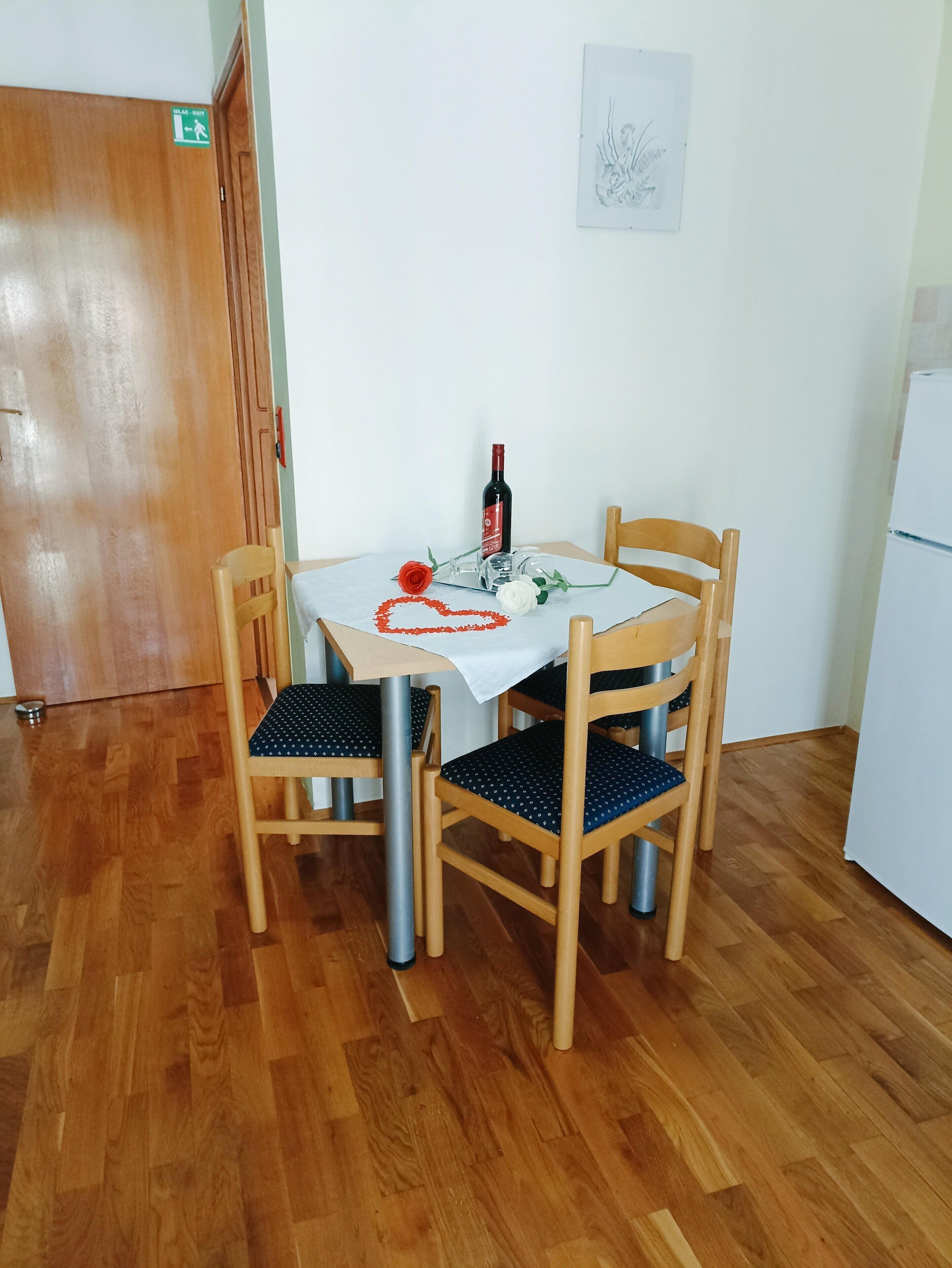 A dining area with a table set for two, featuring a bottle of wine, a glass, and a heart-shaped decoration.