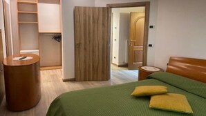 Een slaapkamer met een bed, een houten kledingkast, een klein rond tafeltje en een deur naar een andere kamer.
