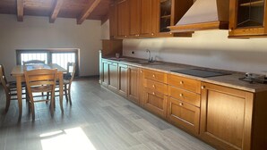 Een keuken met houten kastjes, een groot raam en een eethoek met stoelen.