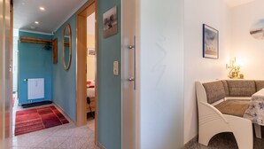 A hotel room with a red carpet, a wooden door, a white bench, and a table with a lamp.