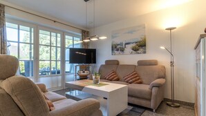 A modern living room with a sofa, a coffee table, a flat-screen TV, and a painting on the wall. - Ferienwohnung für 4 in St. Peter-Ording (St. Peter-Ording)