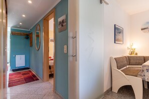 A hotel room with a red carpet, a wooden door, a white bench, and a table with a lamp.