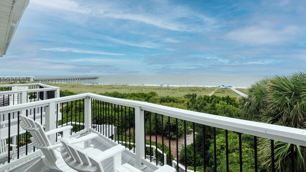 Ein Balkon mit weißen Geländern, der Blick auf einen Strand und einen Steg freigibt.