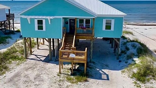 A turquoise beach house with a wooden deck and a staircase leading to a porch.