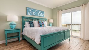 A teal-colored bed with white bedding, two matching nightstands, and a wall sign that reads "you, me + the sea".